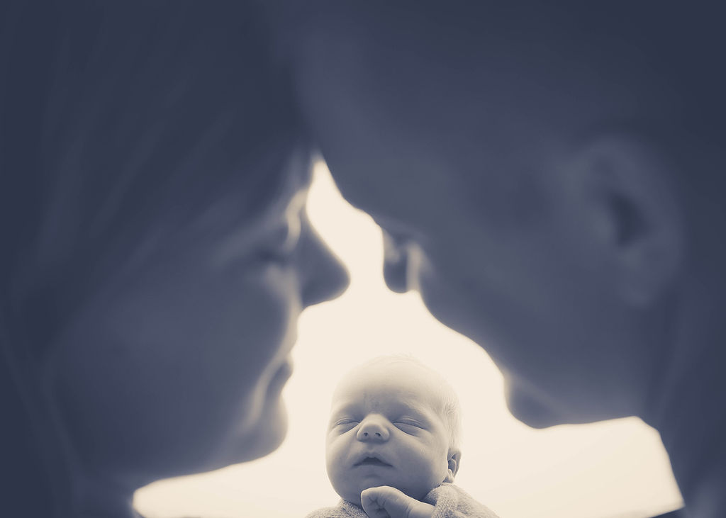 Happy parents snuggle over their sleeping newborn after a parenting class in pella, iowa