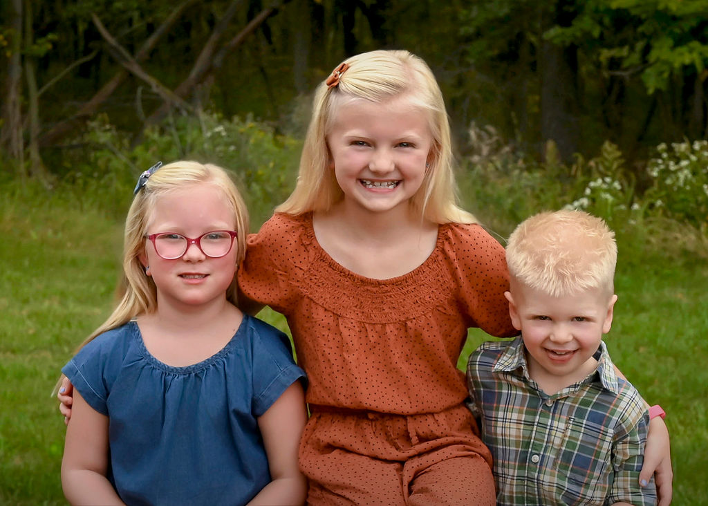 Three happy siblings smile and hug while in a park by a forest