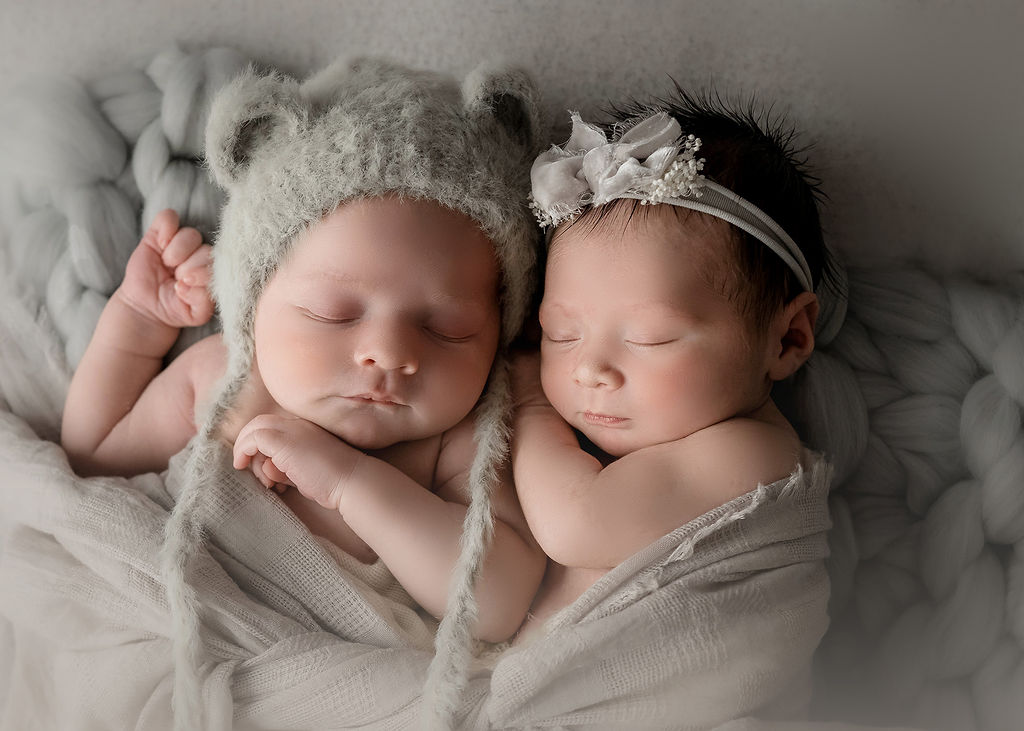 Newborn baby twins snuggle and sleep under cheesecloth blanket