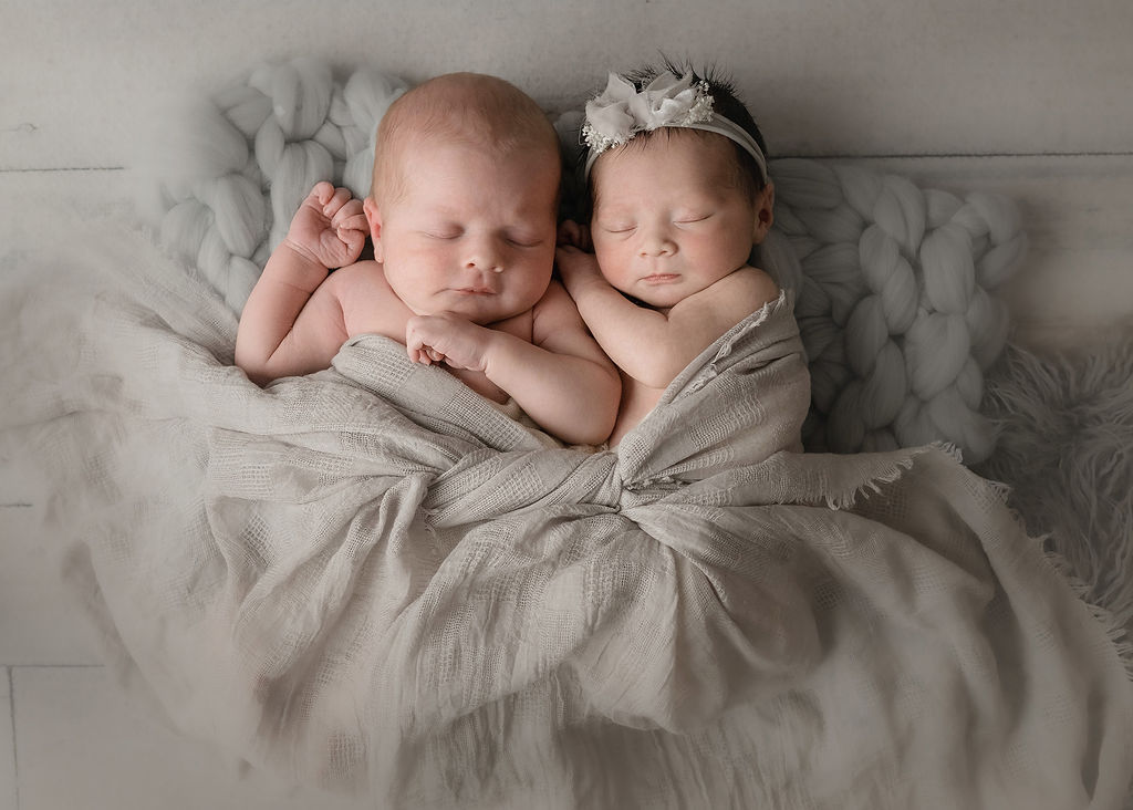 Newborn baby twins sleep and cuddle under a grey blanket in a studio after visiting purple poppy boutique