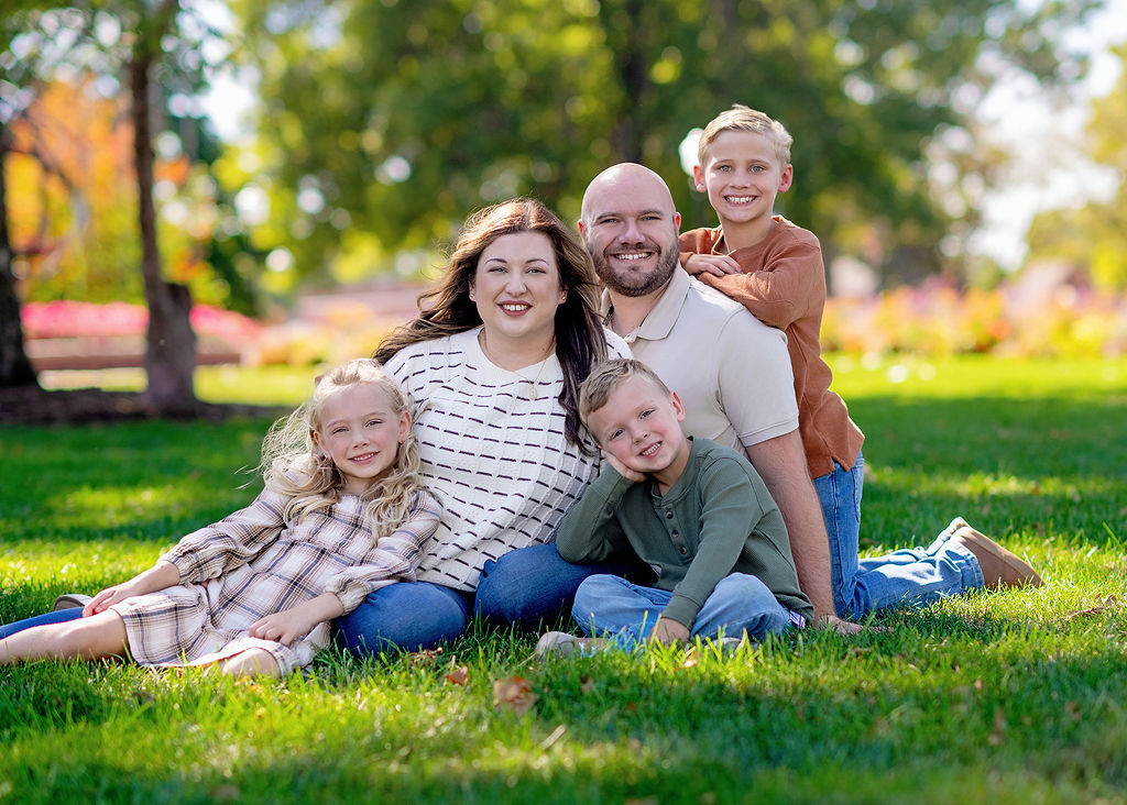 Three young siblings lay and lean on their mom and dad in a park lawn after visiting Robin Riley