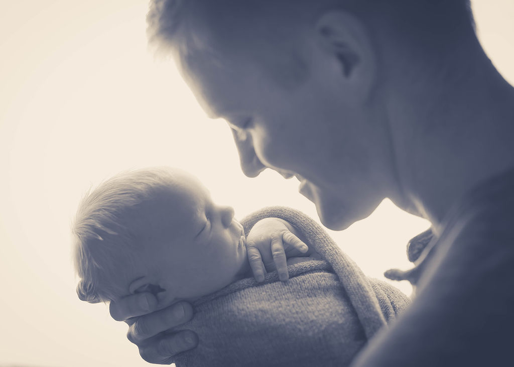 A happy dad smiles down at his newborn baby in his hands