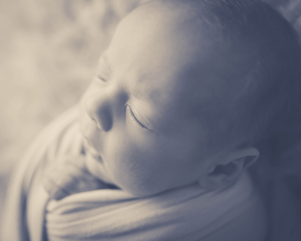 A newborn baby sleeps in a swaddle in black and white before visiting the tongue tie center of iowa